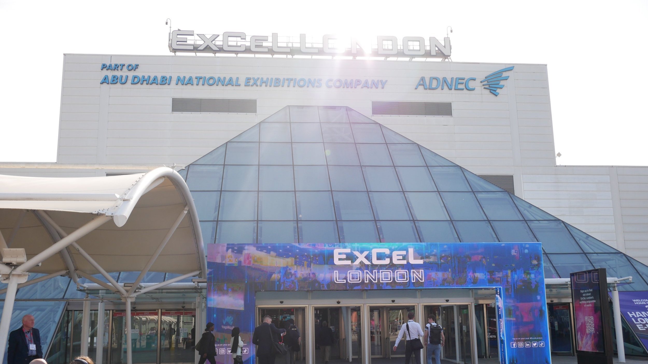The image shows the putside of a big building with a ExCel London sign and banner above the door
