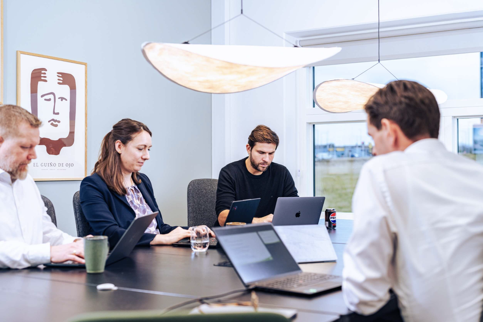 The image shows a professional meeting in progress with four individuals that work at UNIwise around a table. Each person is using a laptop, suggesting a business or collaborative work environment.