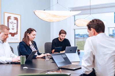 The image shows a professional meeting in progress with four individuals that work at UNIwise around a table. Each person is using a laptop, suggesting a business or collaborative work environment. The image shows a professional meeting in progress with four individuals that work at UNIwise around a table. Each person is using a laptop, suggesting a business or collaborative work environment.