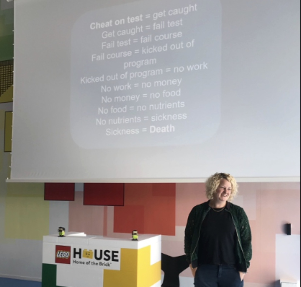 The image shows a woman presenting in front of a big projector screen