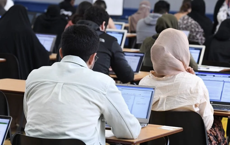Multicultural students taking digital assessment on their laptops in an exam hall